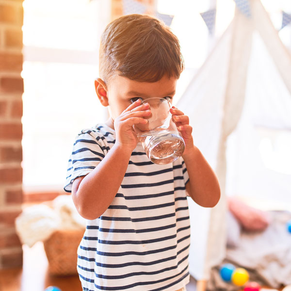 Beautiful toddler boy drinking glass of water at kindergarten